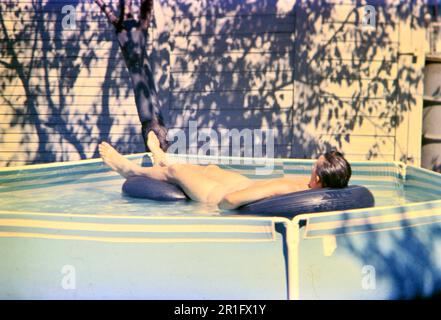 Homme dormant sur un radeau gonflable dans une cour au-dessus de la piscine de terre ca. 1960s Banque D'Images