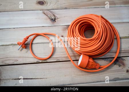 Rallonge électrique de construction orange enroulée sur fond de texture bois. Banque D'Images