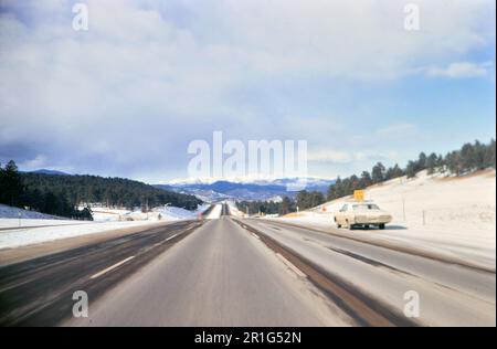 Voiture garée sur le côté d'une autoroute en hiver, montagnes en arrière-plan ca. 1971 Banque D'Images