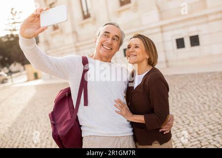 Heureux touristes mûrs conjoints faisant Selfie via smartphone embrassant l'extérieur Banque D'Images