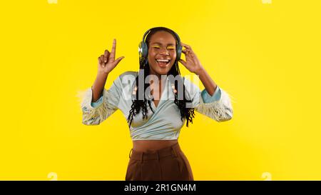 Chanteuse joyeuse de Black Lady portant des écouteurs chantant sur fond jaune Banque D'Images