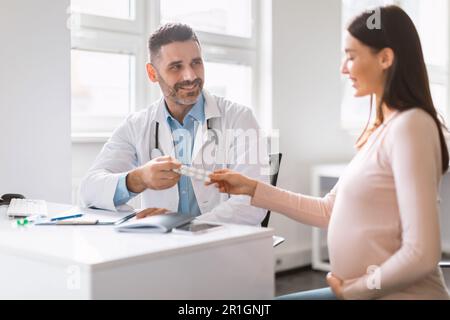 Nutrition pendant la grossesse. Homme spécialiste donnant des vitamines ou des suppléments à la jeune femme enceinte, médecin prescrivant des pilules Banque D'Images