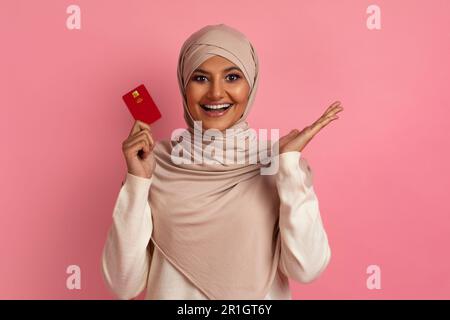 Portrait d'une femme musulmane excitée dans le hijab avec une carte de crédit en main Banque D'Images