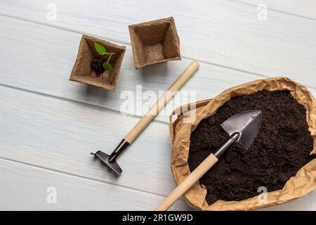 Souillez dans un sac en papier et une pelle sur le dessus. Râteaux et pots de tourbe. Pose à plat. Arrière-plan blanc. Banque D'Images