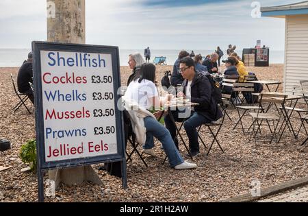 Les gens mangent des crustacés et des fruits de mer traditionnels à côté d'un tableau de prix sur la plage de galets à Brighton, East Sussex, Royaume-Uni. Brighton, un lieu animé et vibrant Banque D'Images