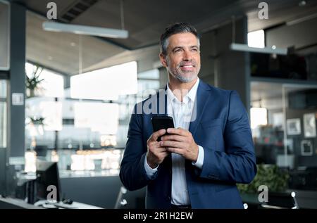 Homme souriant de la moitié de l'âge PDG exécutif porter un costume tenant le téléphone cellulaire au bureau. Banque D'Images