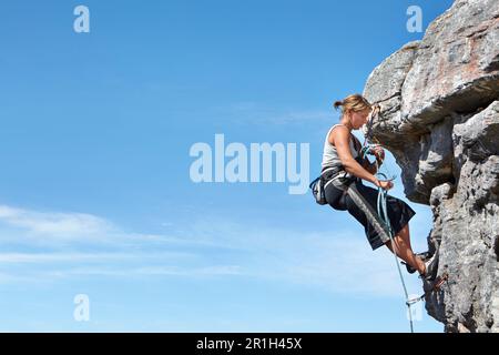 Escalade, ciel bleu et liberté avec une femme sur une falaise de montagne pour l'aventure ou Voyage avec l'espace. Forte, difficile et puissante avec la grimpeur féminine Banque D'Images