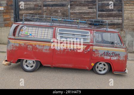 Rayleigh, Royaume-Uni. 14 mai 2023. Une fourgonnette Volkswagen type 2 rouge vieillie avec la marque surf shop est garée dans une rue à Rayleigh, Essex. La fourgonnette dispose de roues personnalisées, d'une suspension abaissée, d'une galerie de toit et de fenêtres à rideaux, évoquant la culture du surf et les voyages nomades. Camion de garage frais de ferme et véhicules américains exposés. Penelope Barritt/Alamy Live News Banque D'Images
