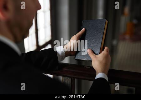 Gros plan du prêtre lisant la Bible pendant la prière debout devant l'autel dans l'église Banque D'Images