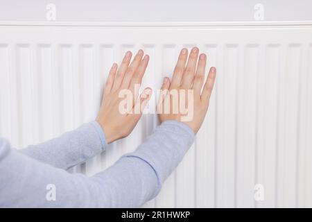 Femme se réchauffant les mains sur le radiateur de chauffage, gros plan Banque D'Images