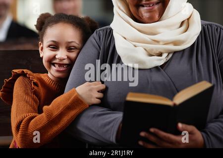 Gros plan de la grand-mère lisant la Bible tout en étant assise sur le banc avec sa petite-fille pendant qu'ils visitent l'église Banque D'Images