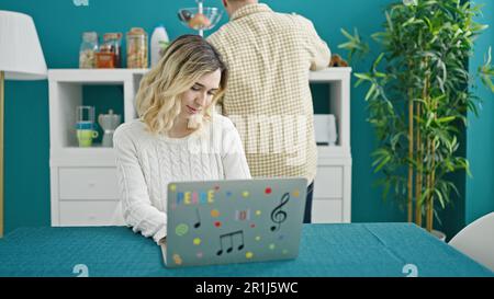 Un homme et une femme sont assis sur une table en utilisant un ordinateur portable pour préparer un café dans la salle à manger Banque D'Images