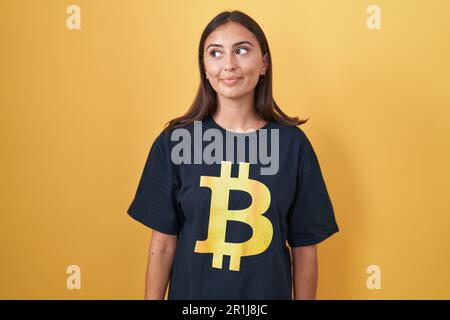 Jeune femme hispanique portant un t-shirt bitcoin souriant regardant sur le côté et regardant loin de penser. Banque D'Images