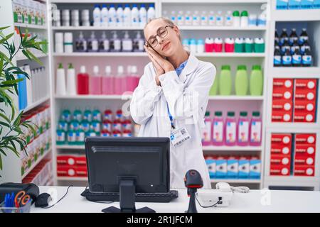 Jeune femme caucasienne travaillant à la pharmacie dort fatigué rêvant et posant avec les mains ensemble tout en souriant avec les yeux fermés. Banque D'Images