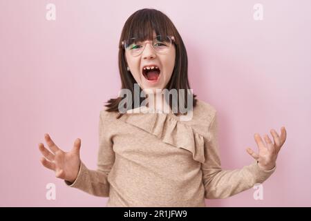 Petite fille hispanique portant des lunettes folle et folle criant et hurlant avec l'expression agressive et les bras levés. concept de frustration. Banque D'Images