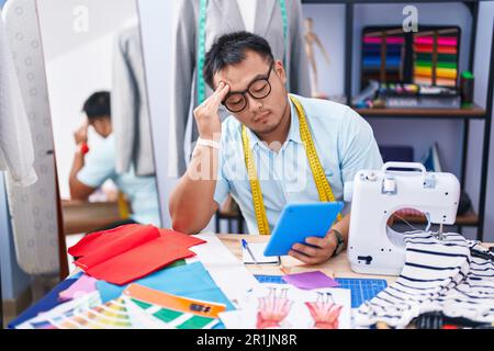 Jeune homme chinois tailleur utilisant le pavé tactile avec une expression sérieuse dans la boutique de tailleur Banque D'Images