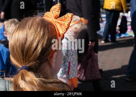 Une fille avec un arc orange dans ses cheveux regarde les gens marcher le jour du Roi ('Koningsdag'), l'anniversaire du Roi Willem-Alexander des pays-Bas Banque D'Images