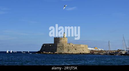 Phare médiéval en pierre dans l'ancien port de l'île de Rhodes, dans la mer Méditerranée. À l'entrée du port sont de petits voiliers Banque D'Images