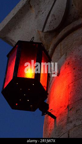 Une lanterne rouge dans un cadre métallique est allumée le soir sur une colonne de pierre à l'entrée du port de l'île. La lanterne est visible en gros plan. Banque D'Images