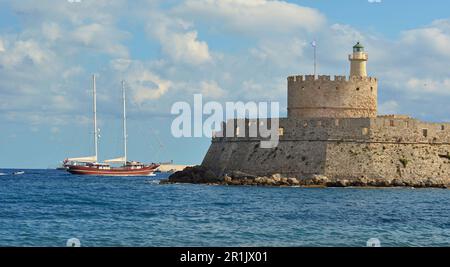 Phare médiéval en pierre dans l'ancien port de l'île de Rhodes, dans la mer Méditerranée. À l'entrée du port sont de petits voiliers Banque D'Images