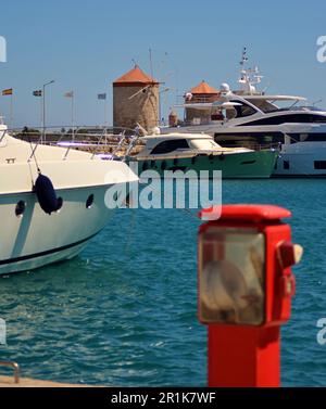 Moulins médiévaux en pierre avec toits rouges dans le port de Rhodes. Les yachts à moteur et à voile sont amarrés au remblai, dans la baie de Mandraki. Banque D'Images