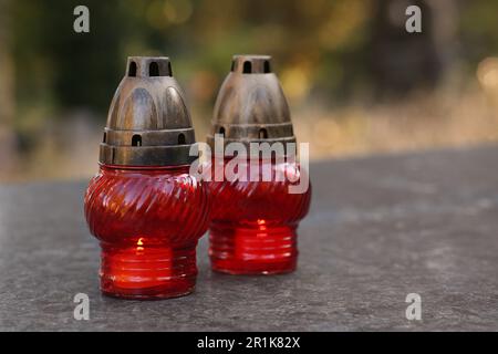 Lanternes de sépulture rouges avec bougies allumées sur la surface de granit dans le cimetière, espace pour le texte Banque D'Images