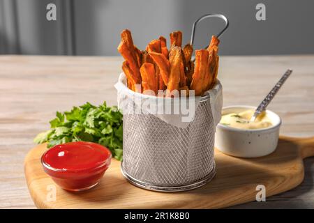 Panier à friture avec frites de patate douce, sauces et persil sur la table Banque D'Images