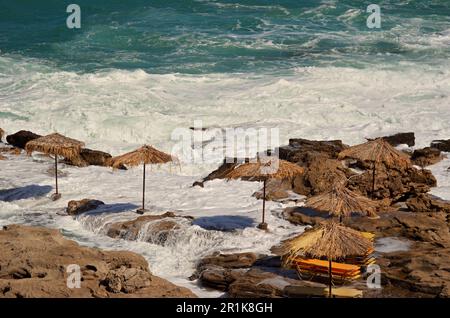 Côte de plage rocheuse en hiver. Fortes vagues de mer blanches, tempête, parasols fermés. Pour chaque parapluie il y a une plate-forme en béton. Banque D'Images