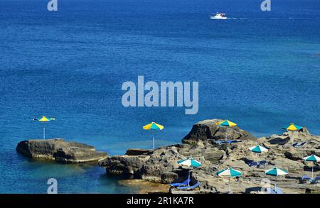 Plage rocheuse avec chaises longues et parasols près de la mer, sur l'île. Les chaises longues sont jaunes et bleues. Parasols en paille à côté des chaises longues Banque D'Images