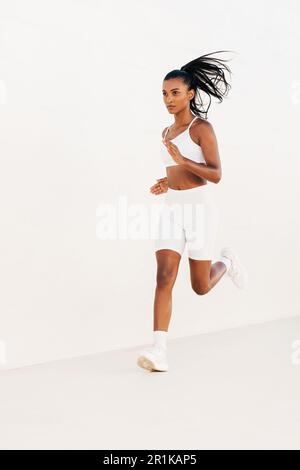 La femme doit faire du jogging à l'extérieur en tenue de sport blanche. Pleine longueur d'une jeune femme sprinting. Banque D'Images