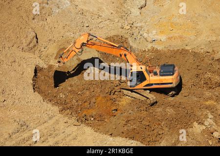 La pelle sur chenilles ramasse la terre avec un godet, vue de dessus. Travaux de terrassement creusant sur un chantier de construction Banque D'Images