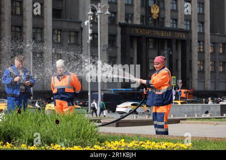 Femme ouvrier arroser la pelouse et les fleurs avec un tuyau sur la place Manezhnaya contre le bâtiment de la Douma d'Etat Banque D'Images