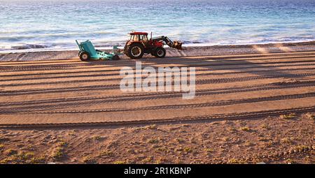 Tracteur avec remorque pour nettoyer la plage des débris d'hiver. Le tracteur travaille sur la mer, près des vagues.le tracteur pose du sable sur la plage. Banque D'Images