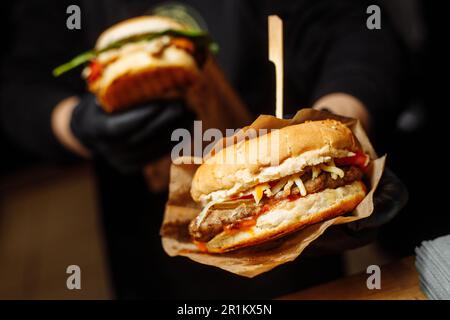 Homme gants noirs tenant les mains de Burger Juicy Burger Fermez le hamburger appétissant. Banque D'Images