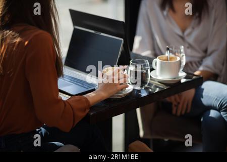 Deux jeunes femmes d'affaires dans un café ayant un sur une réunion. Amis après le travail parlant de gossiping et d'avoir le café à une table de fenêtre avec réflexion Banque D'Images