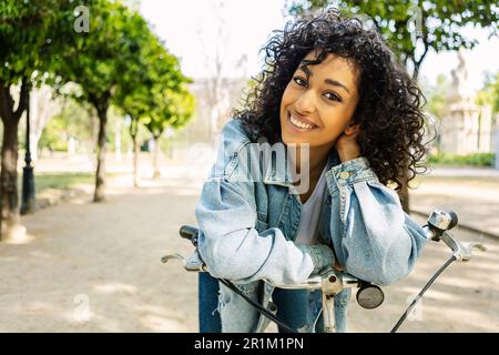 Portrait d'une jeune femme joyeuse à vélo souriant à l'appareil photo du parc de la ville Banque D'Images