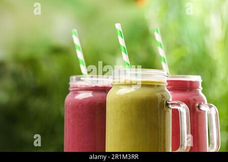 Différents délicieux smoothies dans des pots de maçon sur fond flou, gros plan Banque D'Images