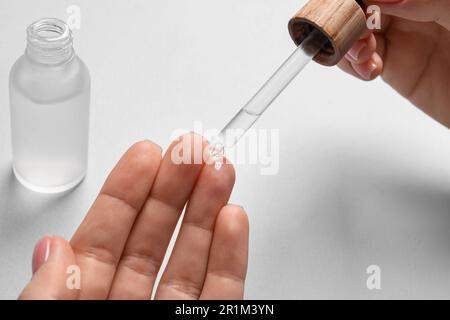 Femme qui goutte du sérum de la pipette sur sa main à la table blanche, en gros plan Banque D'Images