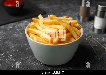 De délicieuses frites fraîches dans un bol sur une table noire, en gros plan Banque D'Images