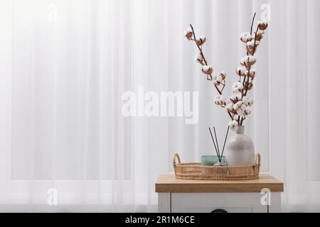 Bougie, diffuseur en roseau et vase avec branches en coton sur commode en bois à l'intérieur. Espace pour le texte Banque D'Images