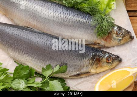 Embarquez avec de délicieux harengs salés, du citron et des herbes sur une table en bois, en gros plan Banque D'Images