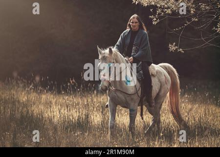 Portrait d'une femme sur sa peinture de guerre indienne d'origine américaine décorée de cheval arabe blanc au printemps en plein air Banque D'Images