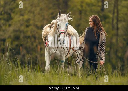 Portrait d'une femme sur sa peinture de guerre indienne d'origine américaine décorée de cheval arabe blanc au printemps en plein air Banque D'Images