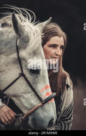 Portrait d'une femme sur sa peinture de guerre indienne d'origine américaine décorée de cheval arabe blanc au printemps en plein air Banque D'Images
