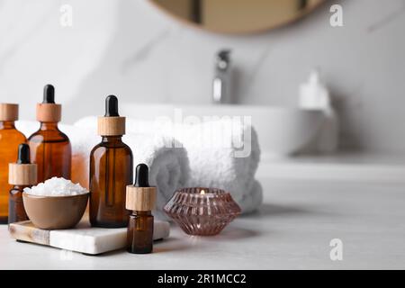 Huiles essentielles, sel de mer, bougie et serviettes sur comptoir blanc dans la salle de bains. Espace pour le texte Banque D'Images