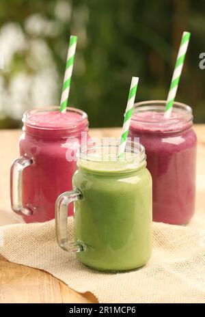 Différents délicieux smoothies dans des pots de maçon sur une table en bois sur fond flou Banque D'Images