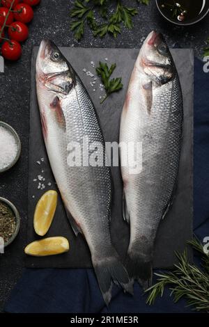 Poisson frais cru de bar de mer et ingrédients sur table noire, plat Banque D'Images