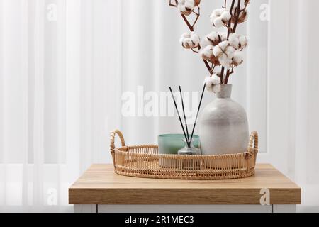 Bougie, diffuseur en roseau et vase avec branches en coton sur commode en bois à l'intérieur. Espace pour le texte Banque D'Images