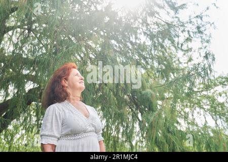 Portrait d'une femme latino-américaine aux cheveux rouges souriant, rêvant de rêver dans la nature. Composition lumineuse avec espace de copie. Concept: La paix de l'esprit et h Banque D'Images
