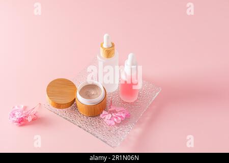 gommage du corps dans un pot en bambou ouvert et deux cosmétiques dans des bouteilles blanches mates avec compte-gouttes pour le soin naturel du visage et du corps de la peau. Fond rose Banque D'Images